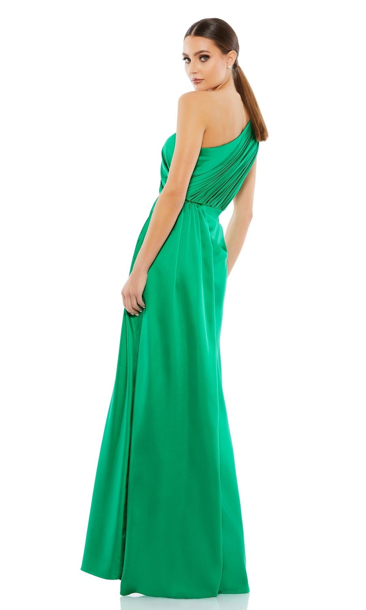 A woman models the Mac Duggal 26654 One-Shoulder Long Formal Dress in green, standing with her back turned and looking over her shoulder against a white background.
